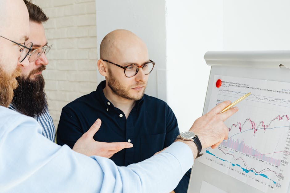Three men discussing financial charts on a whiteboard during a business meeting.