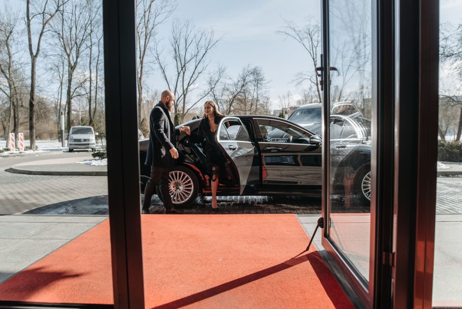 A couple stepping out of a luxury car onto a red carpet in an upscale outdoor setting