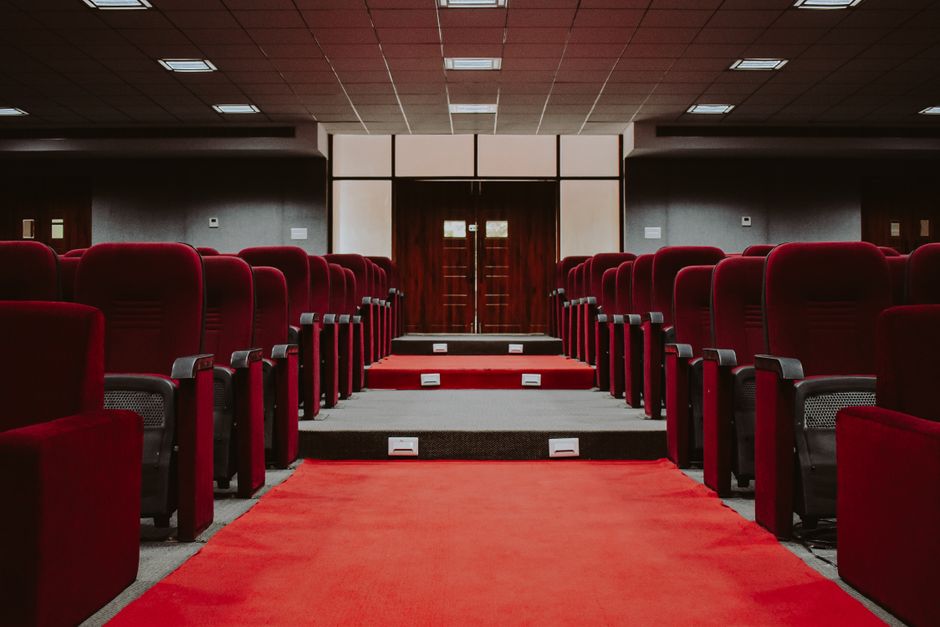A luxurious empty auditorium with rows of red velvet seats and a red carpet aisle